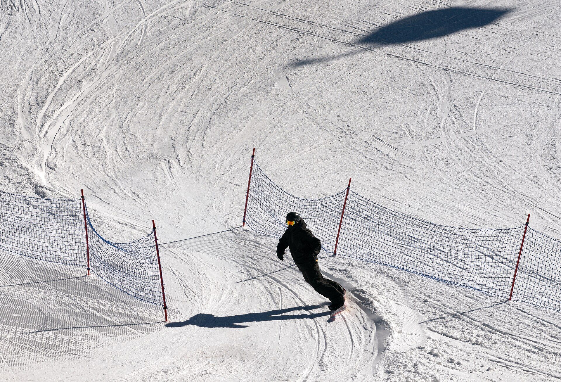 A snowboarder moving across a groomed, fenced learning area at Mammoth Mountain.