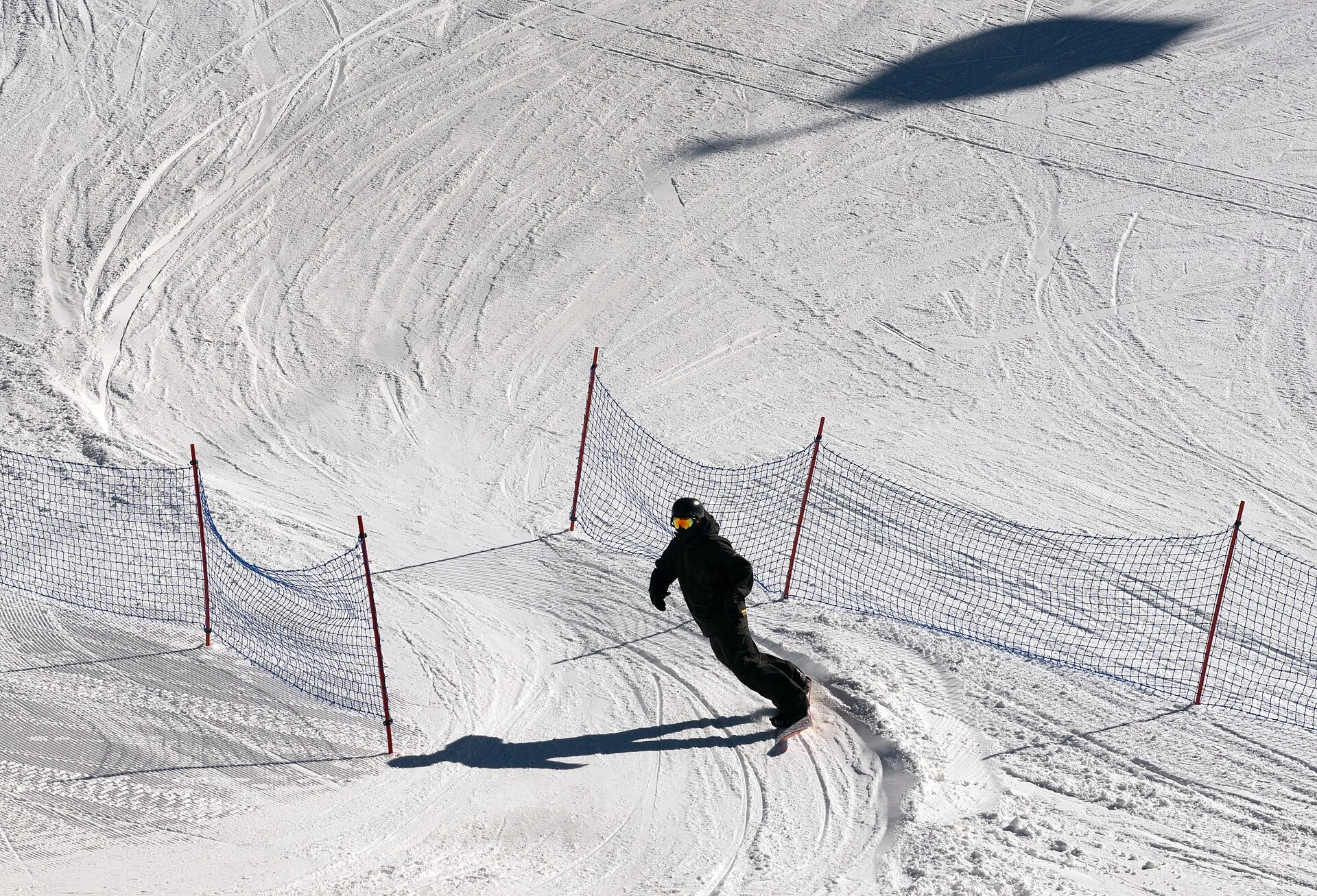 A snowboarder moving across a groomed, fenced learning area at Mammoth Mountain.